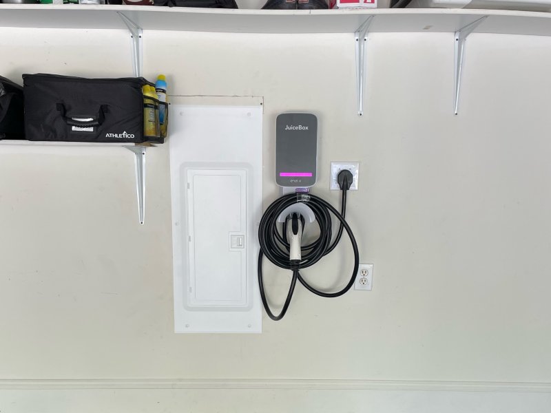 EV Charger hanging on the wall next to white electrical box and items on shelf