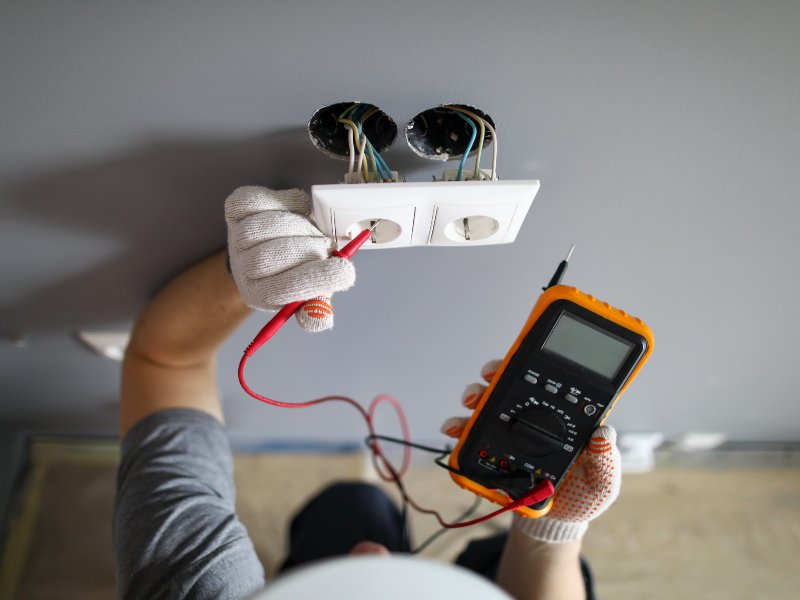 electrician inspects electrical wiring inside a metal panel with a multimeter tool